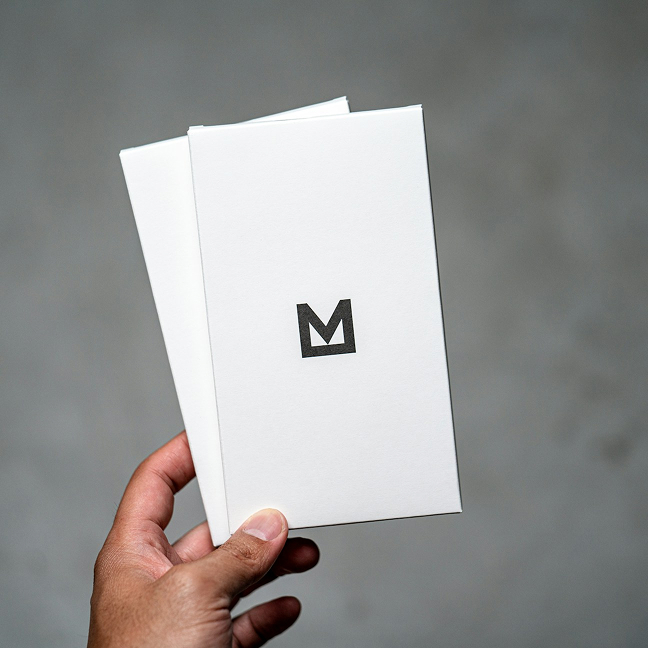 A photo of a hand holding a white card with a black letter M printed on it.