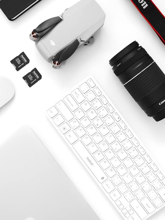 Overhead photo of a keyboard and photography equipment lined up diagonally on a while table